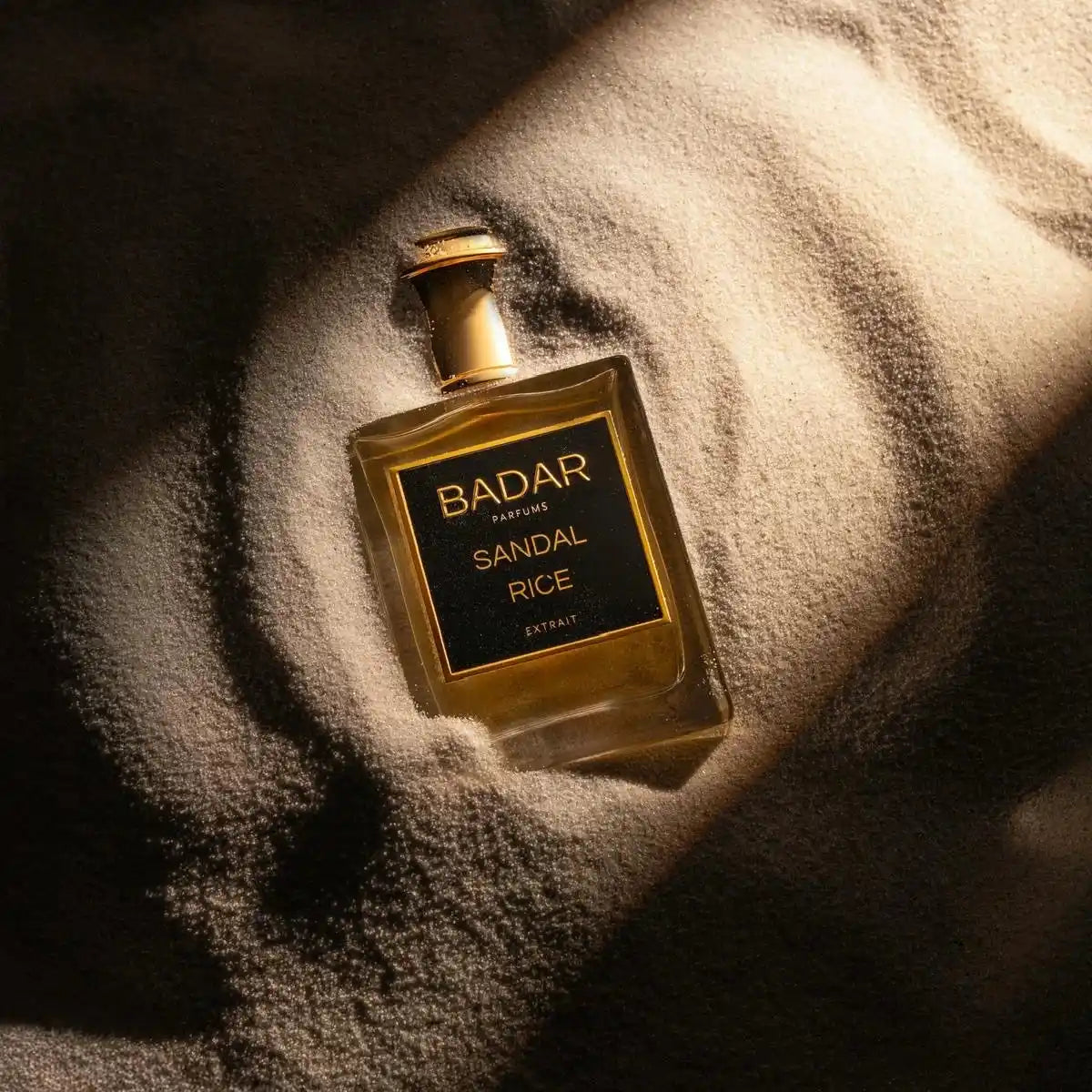 Flacon Sandal Rice de la Maison Badar Parfums dans du sable fin avec la lueur du soleil