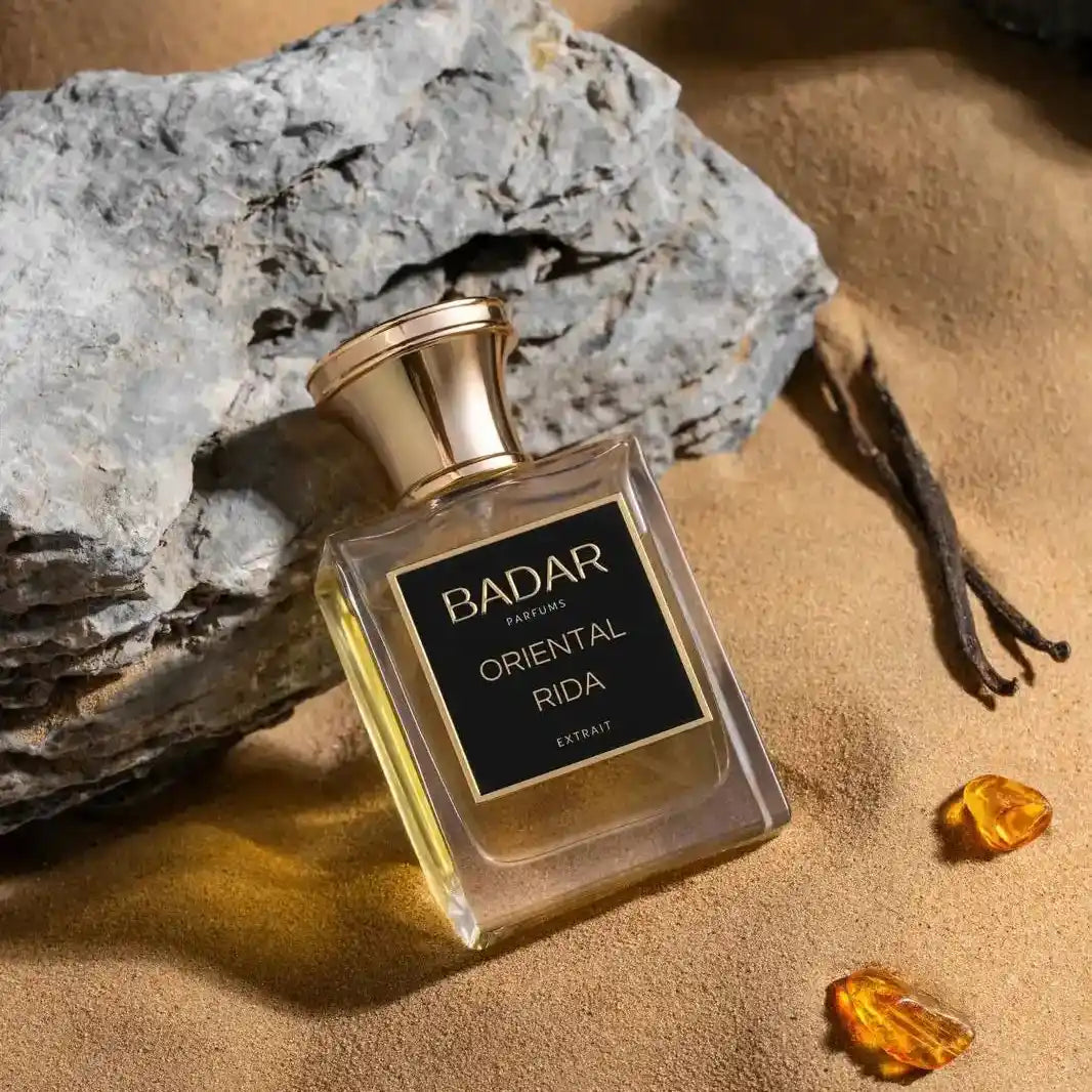 Parfums de niche.Flacon Oriental Rida de la Maison Badar Parfums, sur un rocher gris et du sable fin avec deux pierre d'ambre  et deux gousses de vanille